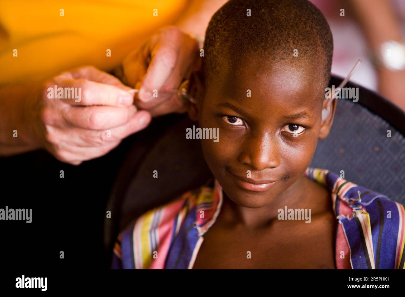 Il fondatore e CEO di SHF si occupa degli apparecchi acustici di un giovane ragazzo del Malawi che ha viaggiato per molte miglia in autobus fino alla missione della Starkey Hearing Foundation Foto Stock