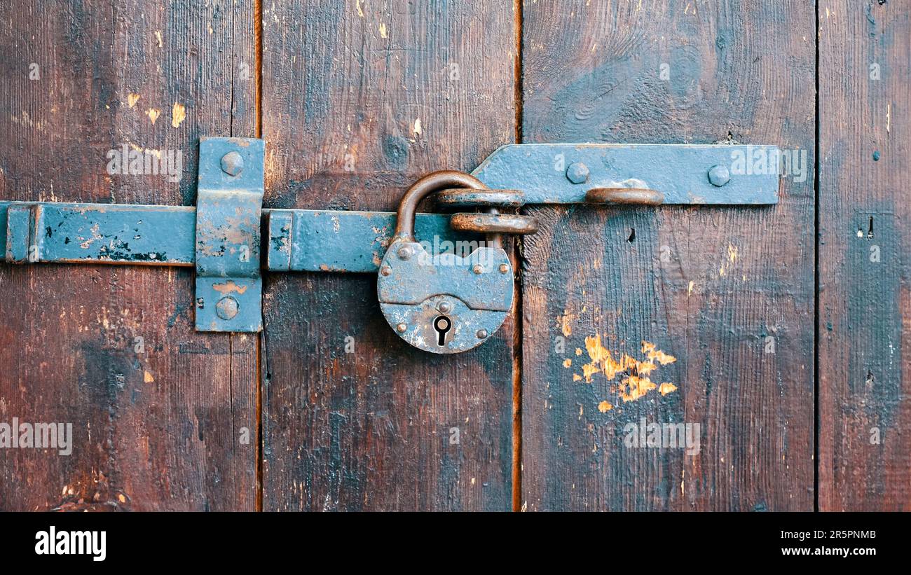 Lucchetto arrugginito su una vecchia porta in legno da vicino Foto Stock