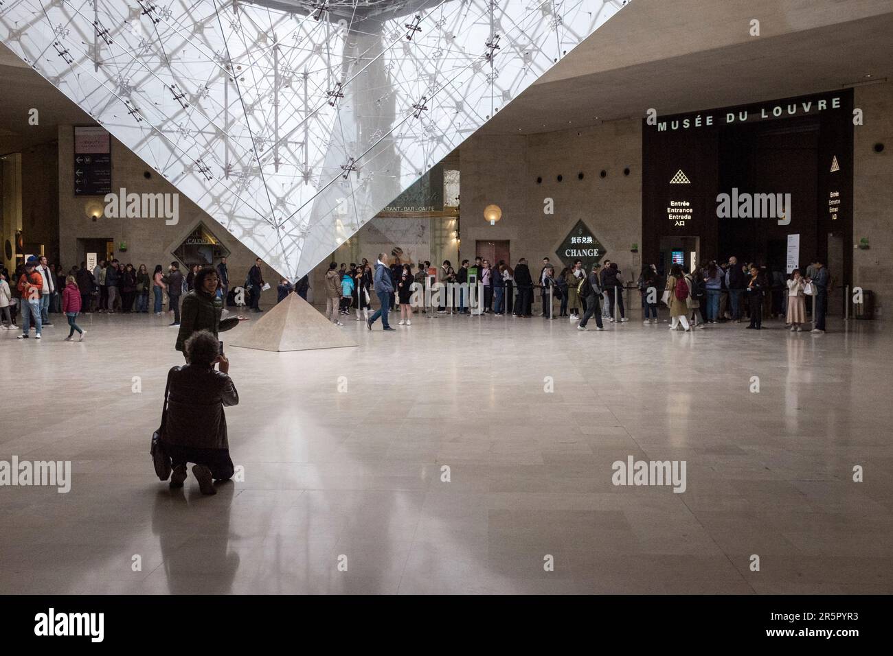 Le persone a Parigi, in Francia, si riuniscono intorno all'accattivante piramide rovesciata situata all'interno del famoso centro commerciale, 'Carrousel du Louvre', mentre le persone si allineano per entrare nel museo sullo sfondo. Foto Stock