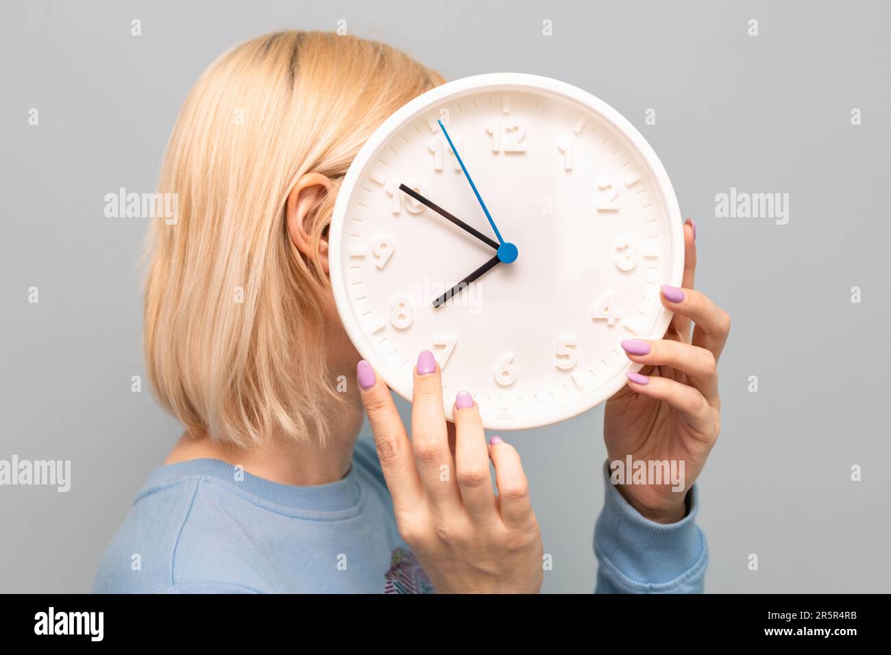 una donna tiene in mano un grande orologio bianco rotondo. il tempo non aspetta. età della persona. orologio invece di una testa. conto alla rovescia. Foto di alta qualità Foto Stock