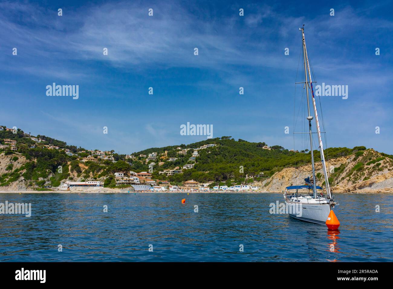 Javea, Alicante, Spagna. 22 maggio 2022 - Una barca a vela ancorata di fronte alla baia, Cala Portichol, una piccola spiaggia con edifici di pesca e costiero Foto Stock