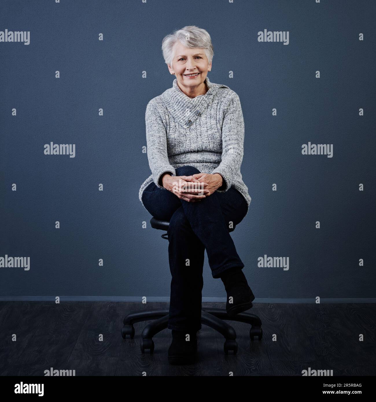 L'età è solo un numero. Studio shot di una donna anziana allegra seduta con le gambe incrociate mentre guardava la macchina fotografica. Foto Stock