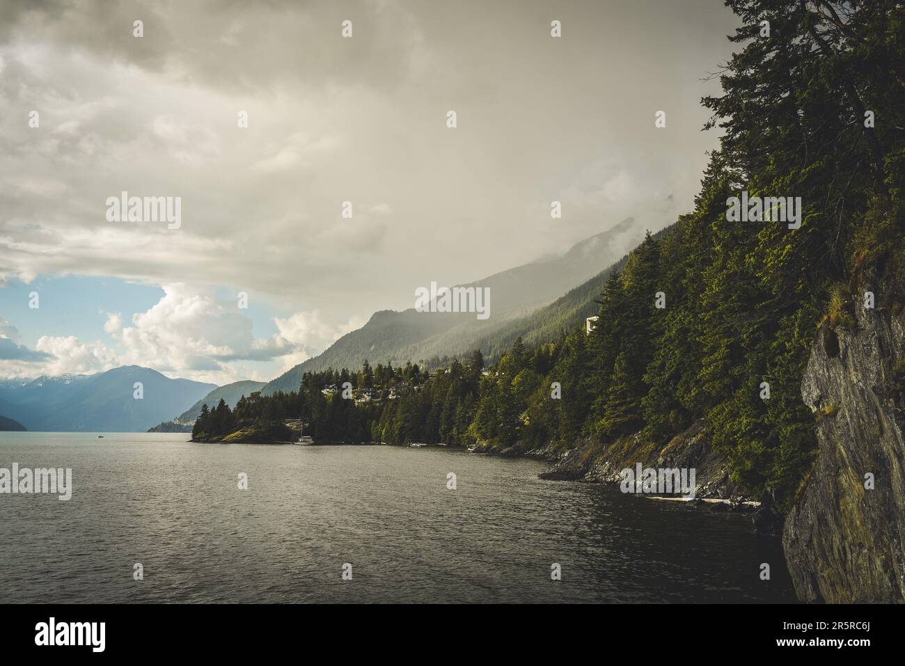 Nuvole di Moody sull'acqua calma in Howe Sound vista dalla zona di Lions Bay nel nord di Vancouver con montagne rocciose sullo sfondo Foto Stock