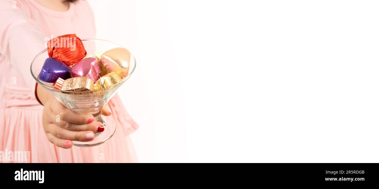 Ragazza che tiene una tazza di vetro di caramelle. Offre cioccolato colorato avvolto. Design tradizionale dello striscione ramadan Feast Concept. Sfondo bianco isolato. Foto Stock