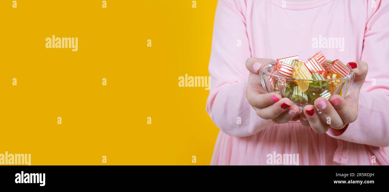 Ragazza con caramelle rigide colorate per lo striscione del banchetto dello zucchero. Sfondo studio giallo, spazio copia. Saluto, celebrazione del concept design religioso. Foto Stock