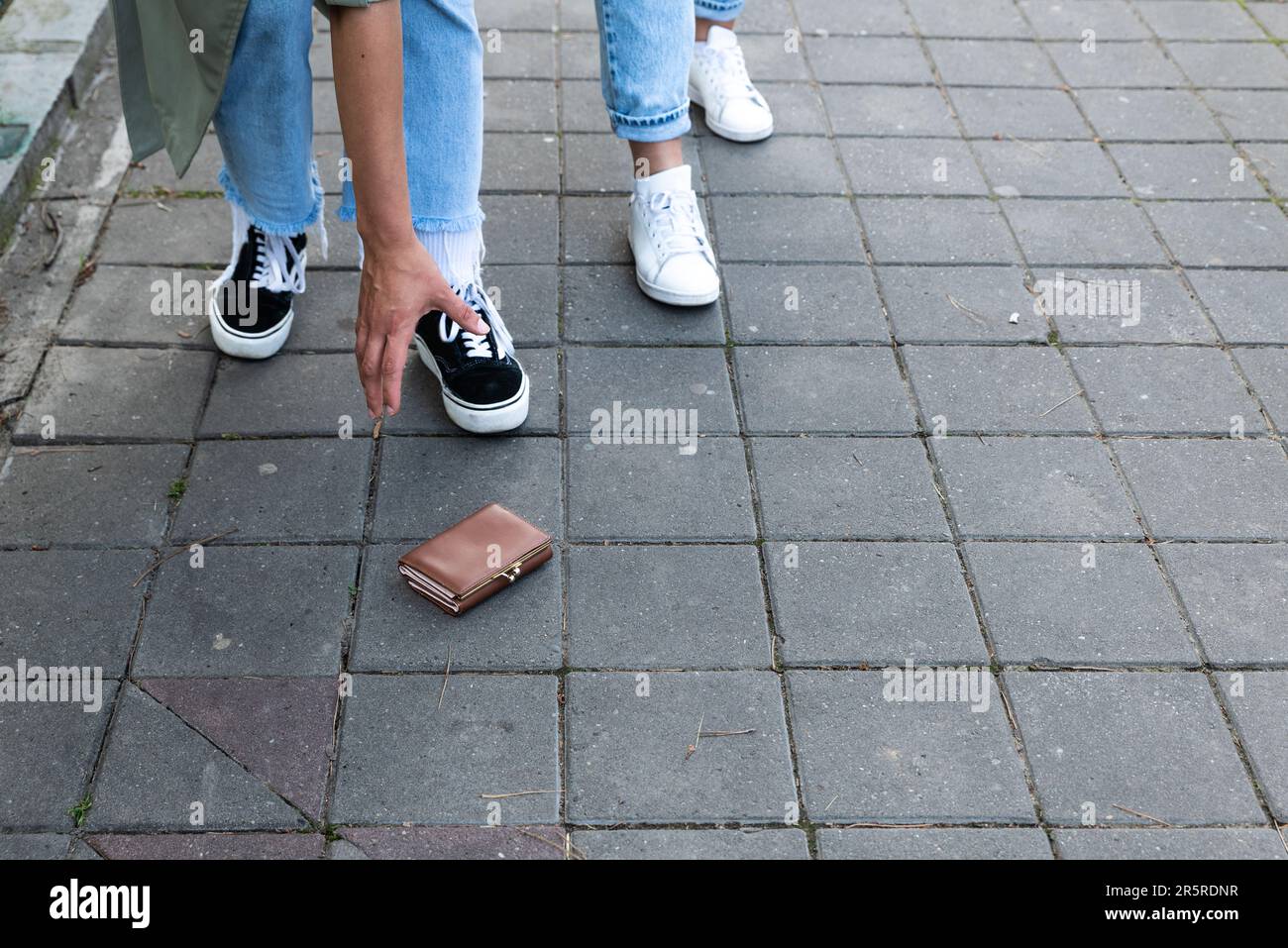 Due donne pedoni trovano un portafoglio perso sul marciapiede in una zona pedonale in una strada della città qualcuno lo ha lasciato cadere dalla loro tasca o da purs Foto Stock