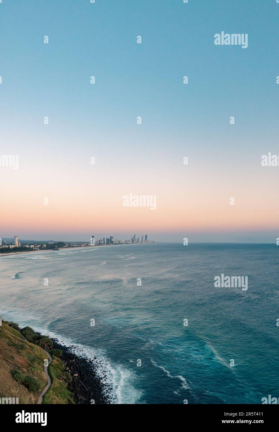 Una vista aerea di un vivace skyline cittadino che guarda alla costa, con lussureggianti colline verdi che si affacciano sull'oceano blu scintillante Foto Stock