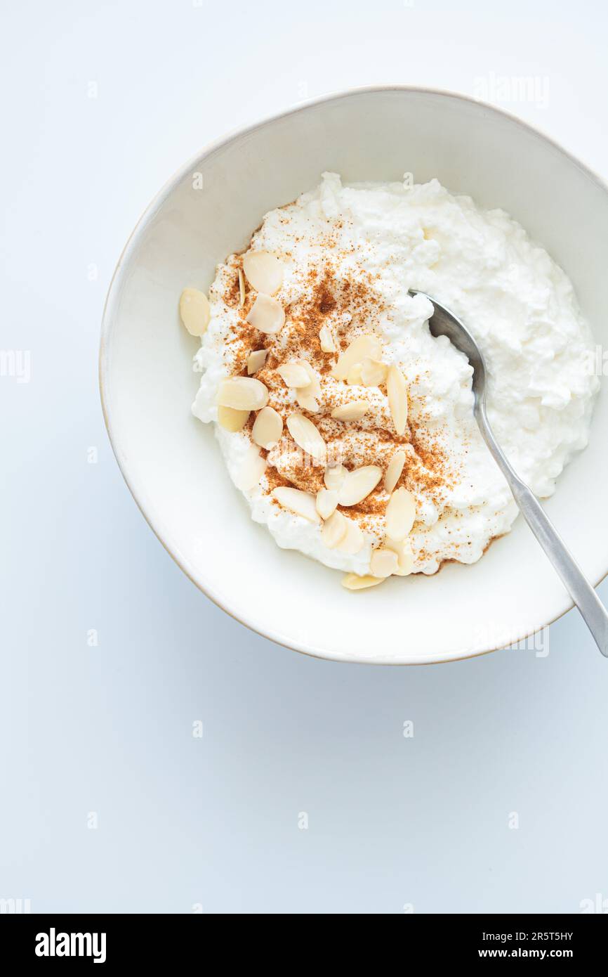 Cottage formaggio con cannella e mandorle in una ciotola bianca, sfondo bianco, vista dall'alto. Concetto di colazione a base di proteine sane. Foto Stock
