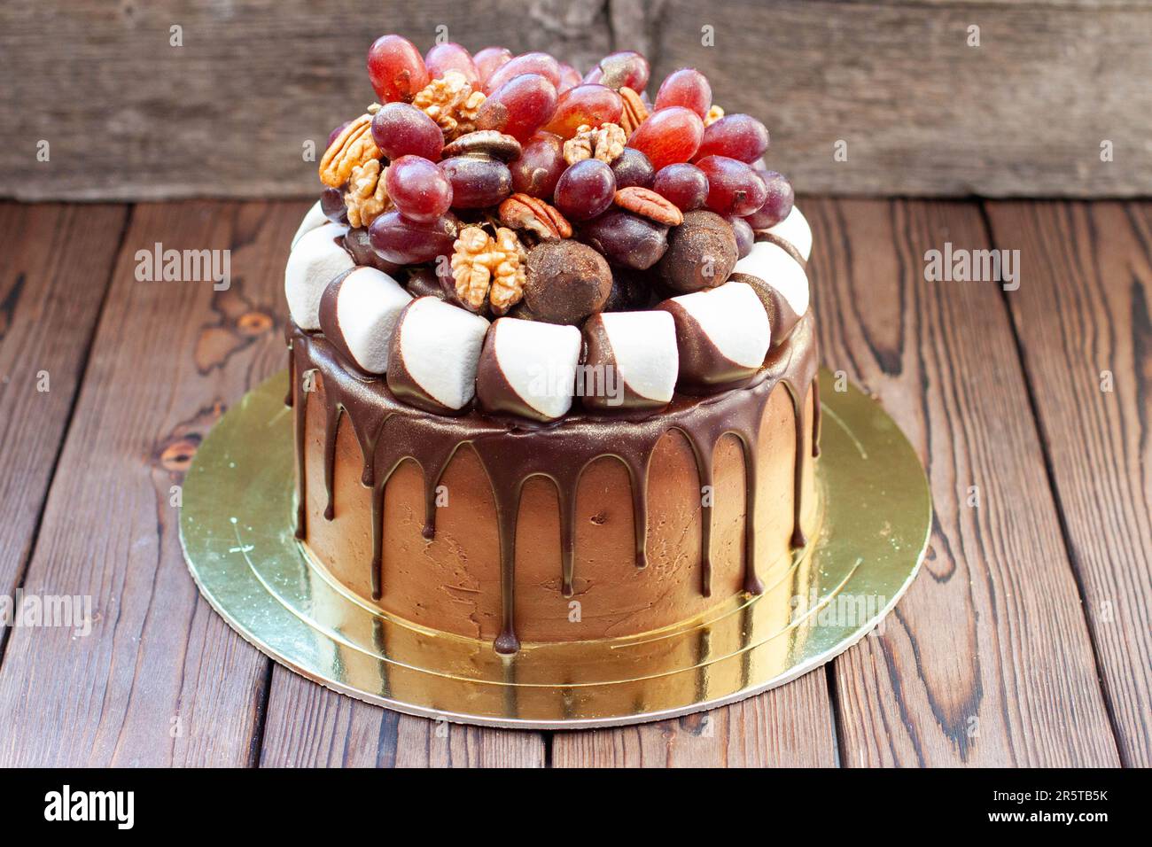 L'idea di torta autunnale fatta di cioccolato e decorata con uva, noci, tartufi al cioccolato e marshmallow. Rustico backgrond, cibo comfort Foto Stock