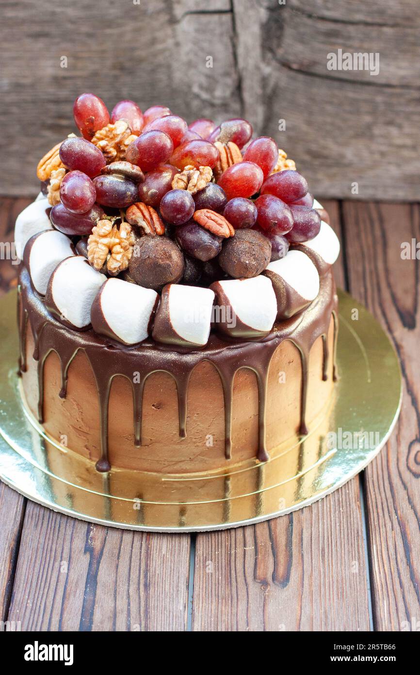 L'idea di torta autunnale fatta di cioccolato e decorata con uva, noci, tartufi al cioccolato e marshmallow. Rustico backgrond, cibo comfort Foto Stock