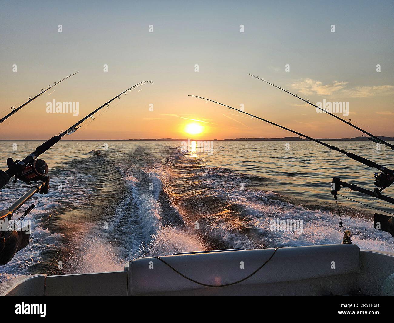 Canne da pesca su una barca a motore con la scia della barca e l'alba cielo sopra l'orizzonte Foto Stock