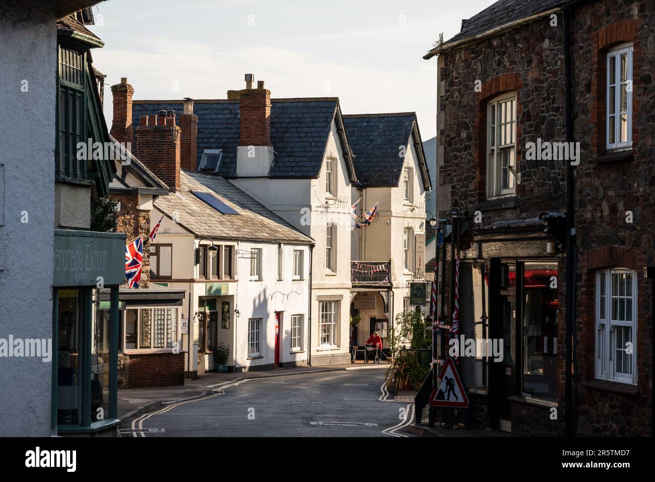 La luce del mattino cade sui negozi tradizionali e sulle case di Porlock High Street sotto le colline di Exmoor sul Somerset occidentale. Foto Stock