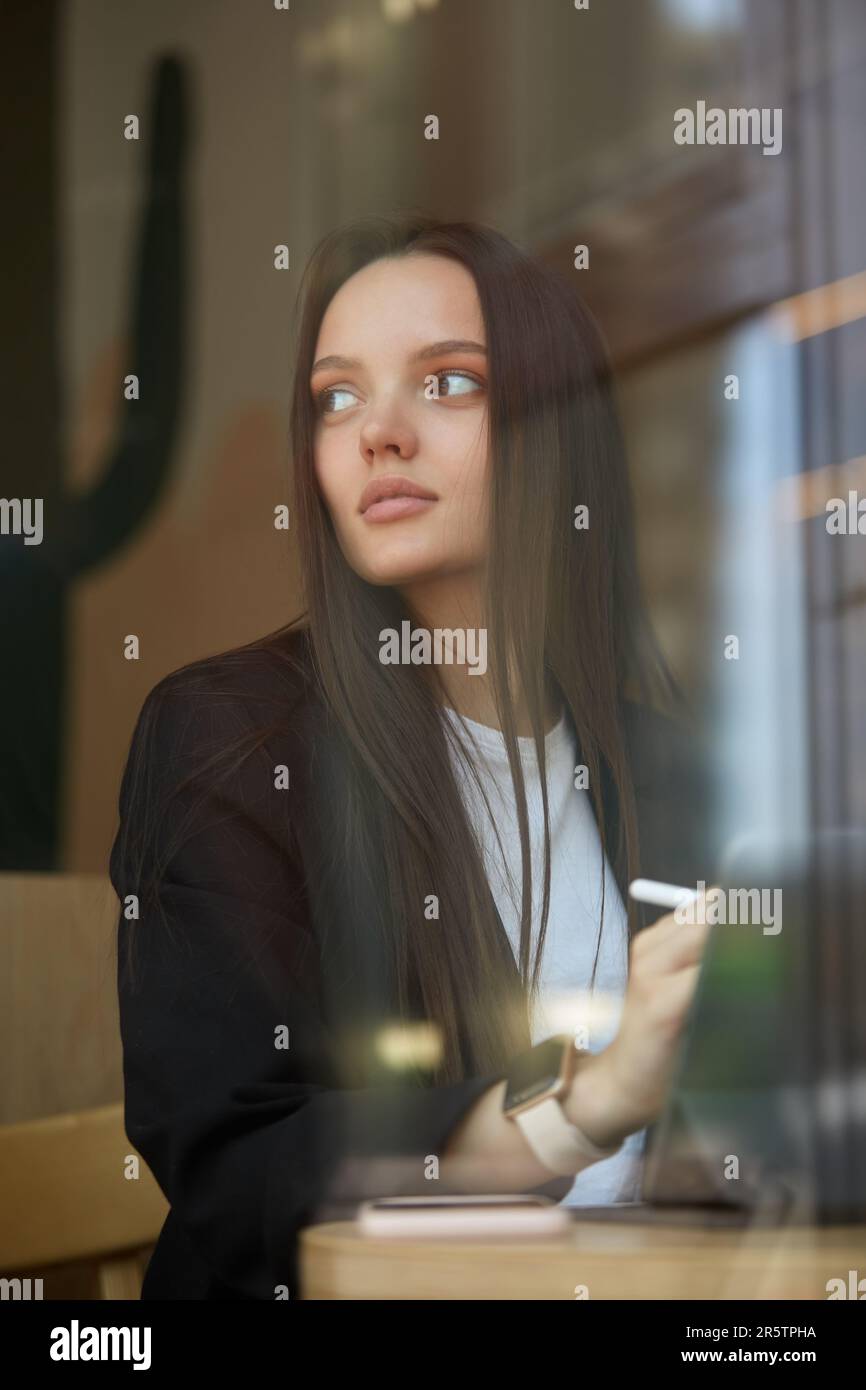 Ritratto di una bella giovane donna seduta in un bar e disegnando un'illustrazione su un computer tablet con una penna stilo. Grafico freelance w Foto Stock