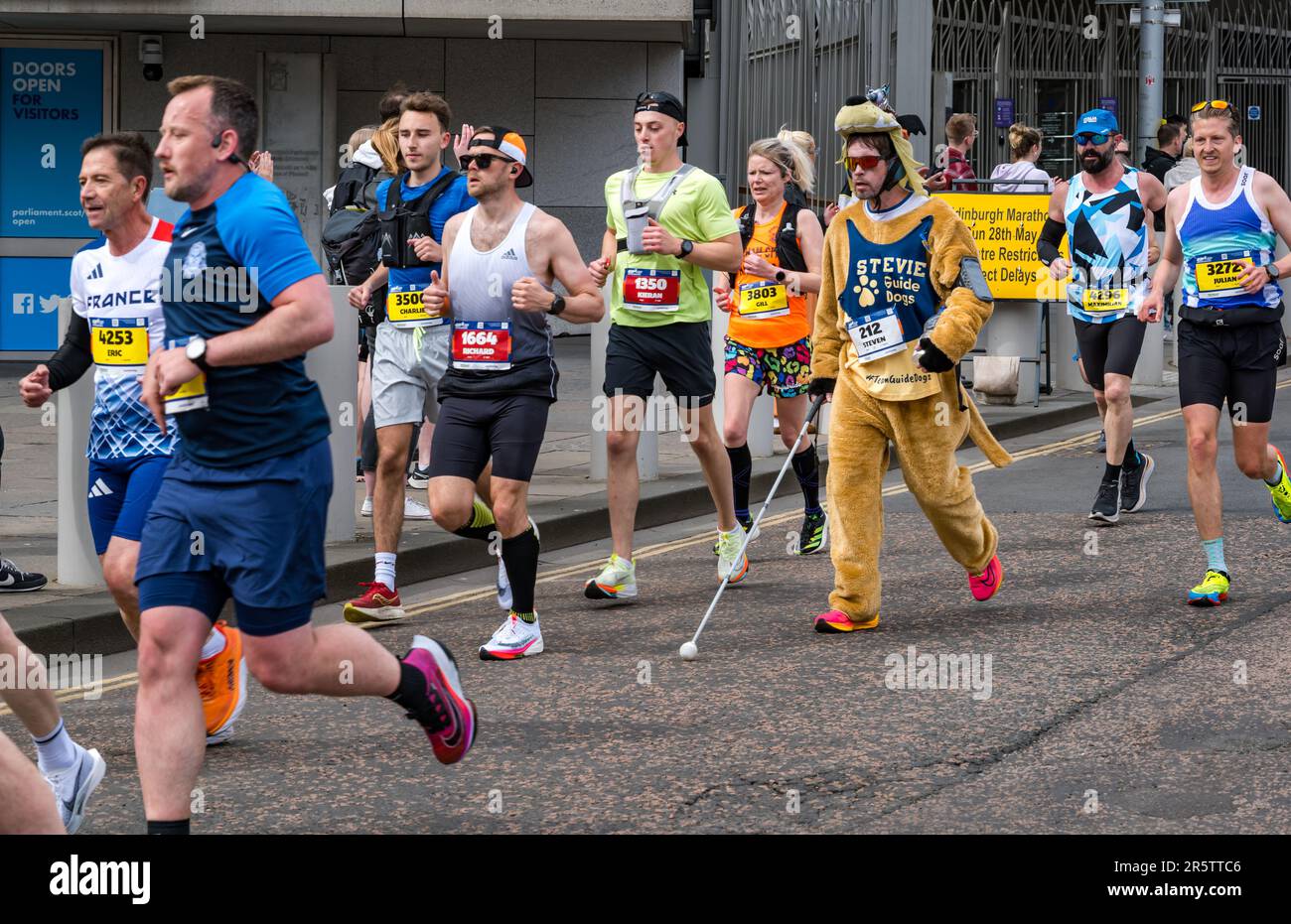 Corridori che corrono nella maratona di Edimburgo 2023 con un corridore di beneficenza cieca disabile in costume da abito di fantasia, Royal Mile, Scozia, Regno Unito Foto Stock