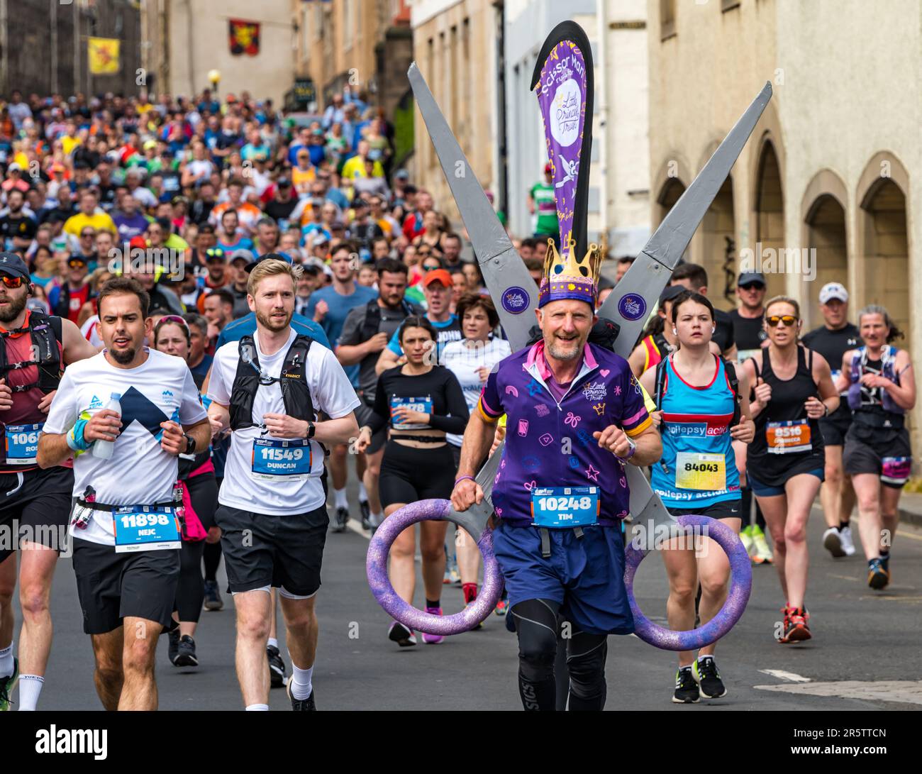 Grande folla di corridori che corrono nella maratona di Edimburgo 2023 con un corridore benefico in costume stravagante, Royal Mile, Scozia, Regno Unito Foto Stock