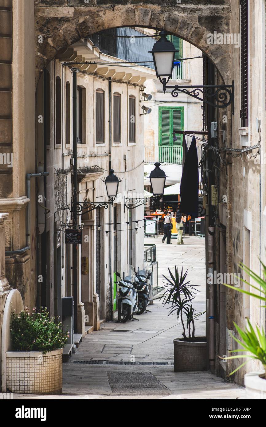 Strada stretta nel centro storico di Bari, Puglia, Italia con edifici storici in pietra, archi e lampioni, verticale Foto Stock
