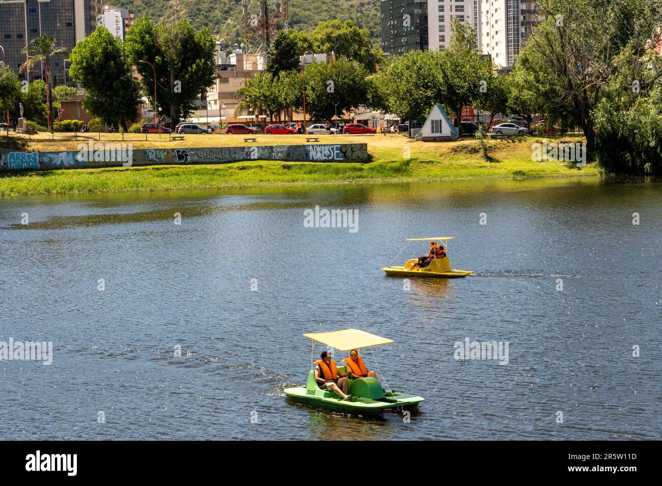 Due persone in kayak stanno godendo l'atmosfera tranquilla di un lago tranquillo, con alberi lussureggianti e cieli azzurri chiari visibili sullo sfondo Foto Stock