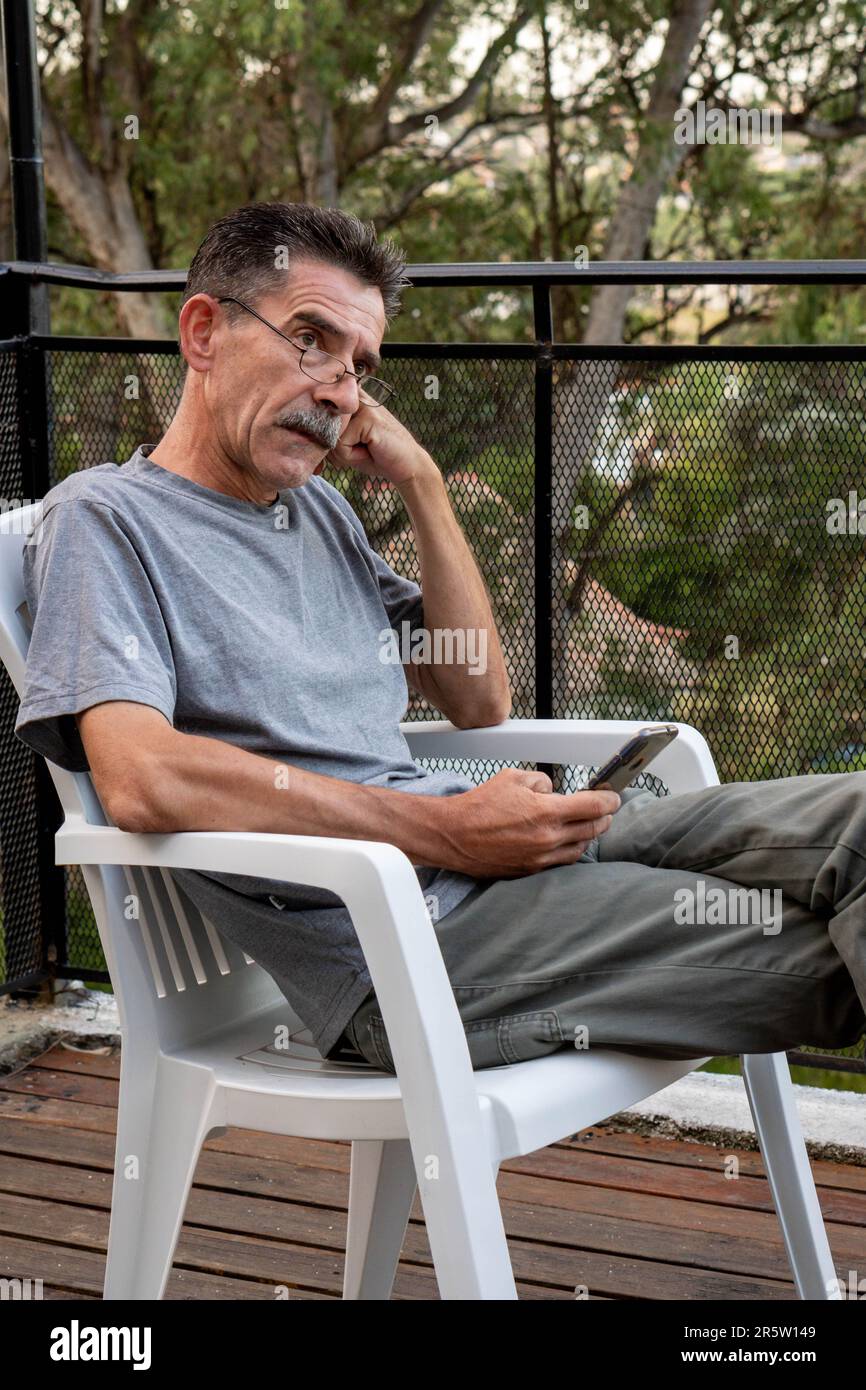 Un giovane adulto maschio è seduto su una sedia in un ambiente home Office, lavorando su un computer portatile e inviando messaggi su un telefono cellulare Foto Stock