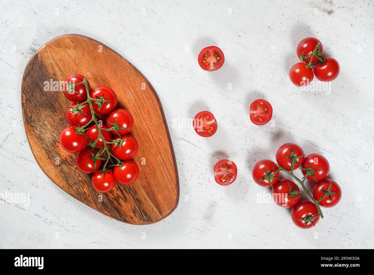 Pomodori rossi animati con vigne verdi su tagliere di legno, tavolo in pietra bianca sotto, vista dall'alto Foto Stock