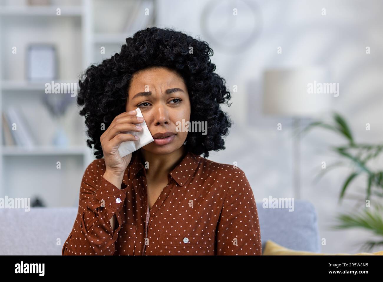 Primo piano. Ritratto di giovane afroamericana sconvolta seduta sul divano a casa e piangendo, soffriva di depressione, strappando lacrime con tovagliolo. Foto Stock