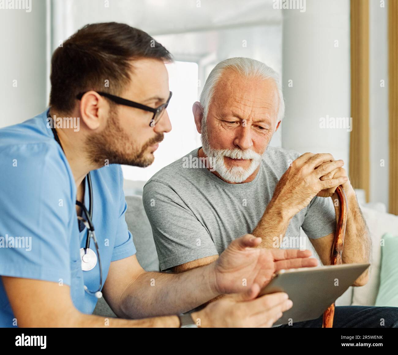 medico infermieristico assistenza senior tablet tecnologia che mostra caregiver aiuto assistenza pensione casa infermieristica anziani felice ridere uomo Foto Stock