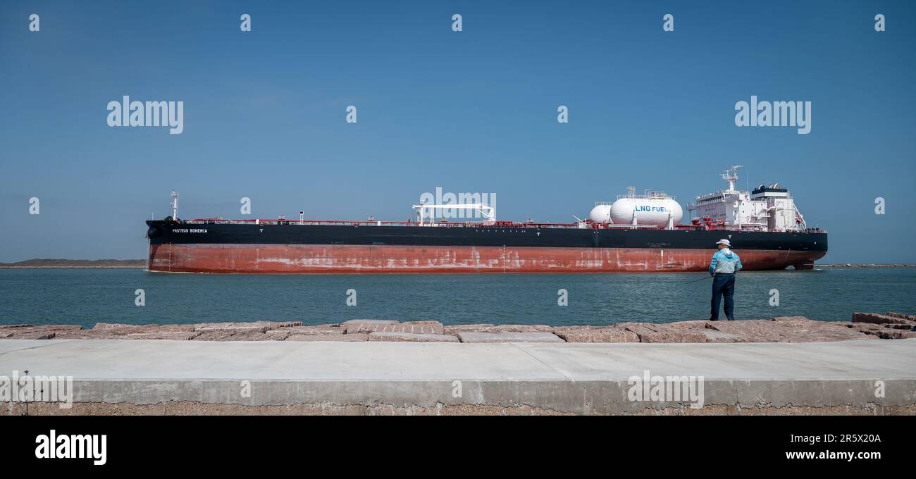 PORT ARANSAS, TX - 26 FEB 2023: Un pescatore sul South Jetty come PROTEUS BOHEMIA, una nave petrolifera grezza naviga dentro dal Golfo del Messico sulla Th Foto Stock