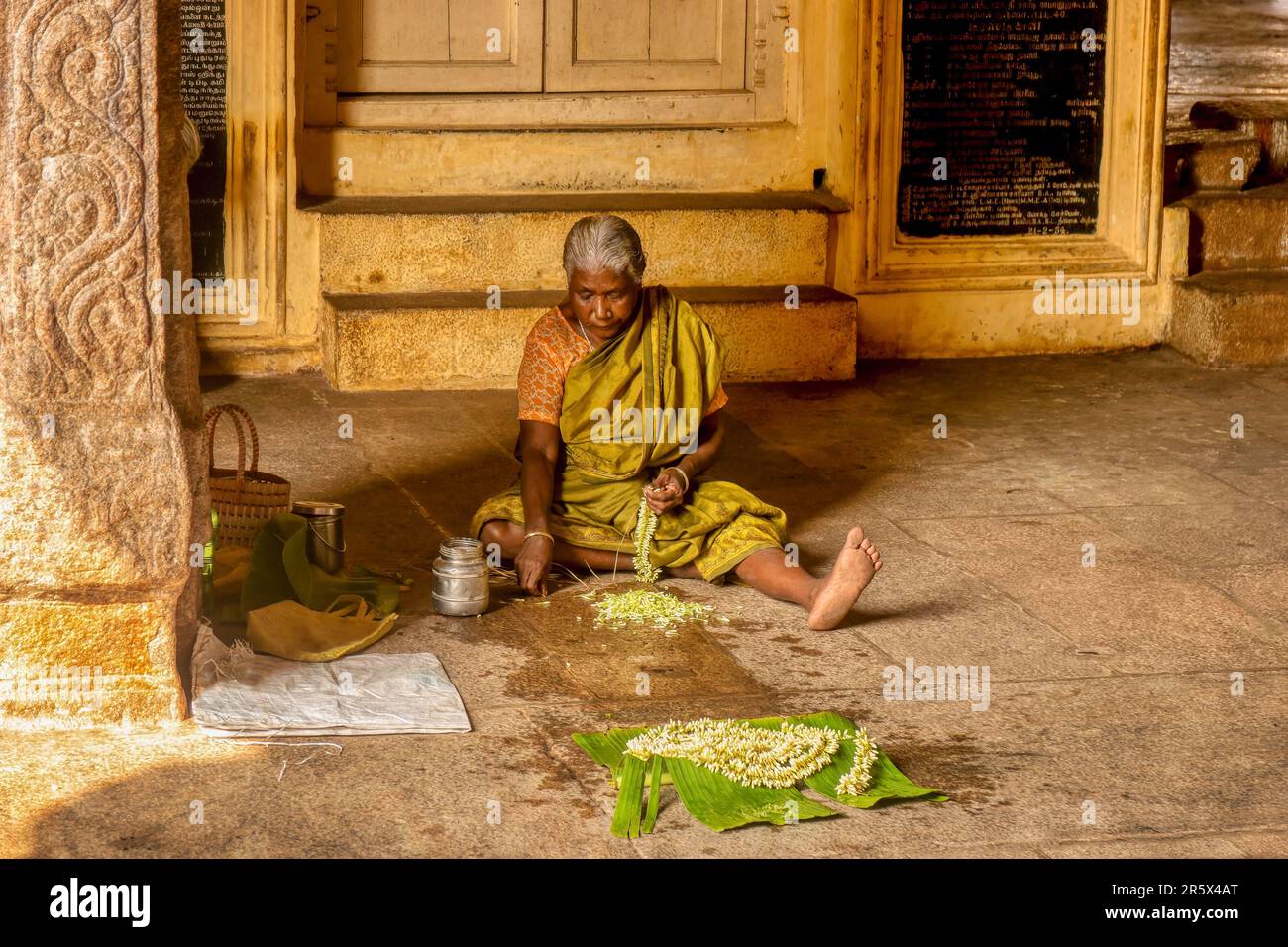 Madurai, Tamil Nadu, India - 10 dicembre 2013. Un indiano anziano siede sul pavimento di un tempio indù che stringe i fiori tradizionali del gelsomino da vendere. Foto Stock