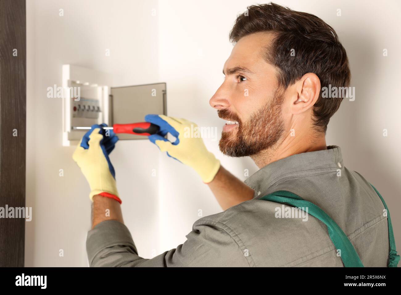 Elettricista che installa la scatola dei fusibili con un cacciavite in interni Foto Stock