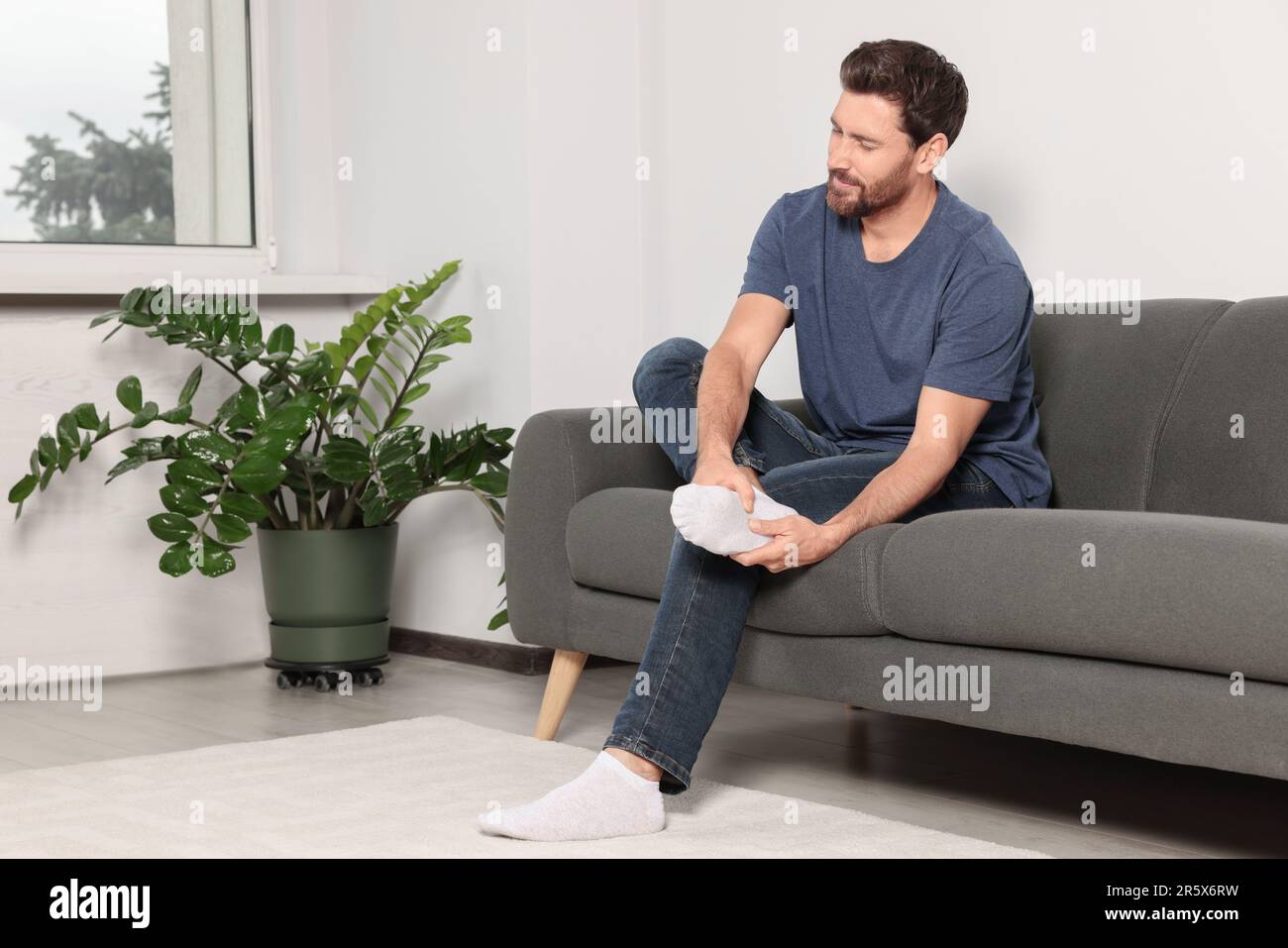 Uomo che soffre di dolore alle gambe e di massaggio del tallone sul divano a casa Foto Stock