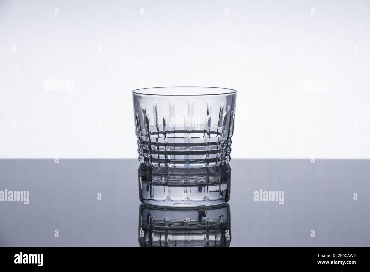 Cristallo di whiskey su una superficie riflettente. Oggetto isolato. Sfondo moderno e suggestivo. Design contemporaneo. Foto Stock