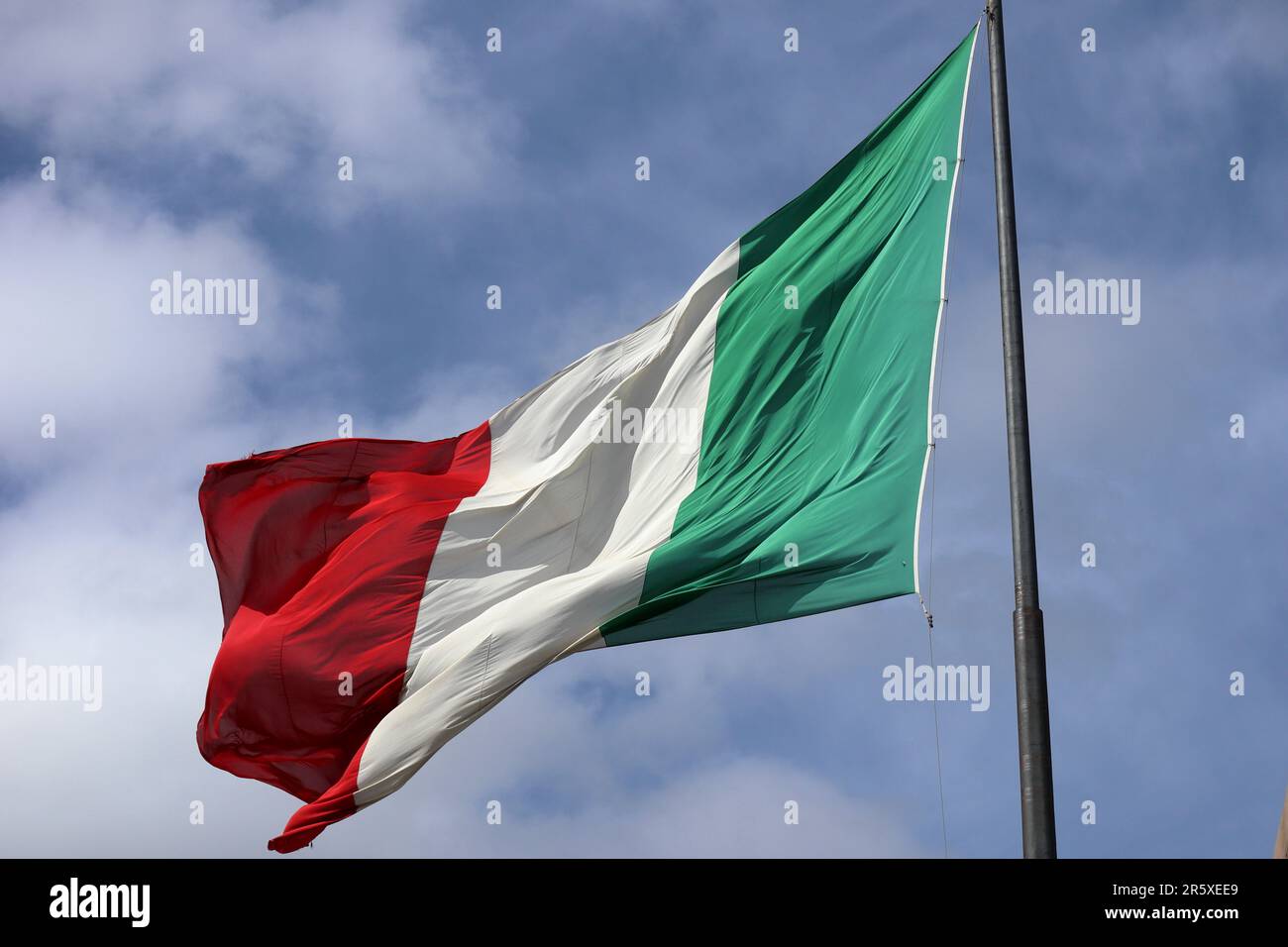 Bandiera dell'Italia che soffia in bright sole mediterraneo su un pennone in piedi in italiano cielo blu Foto Stock
