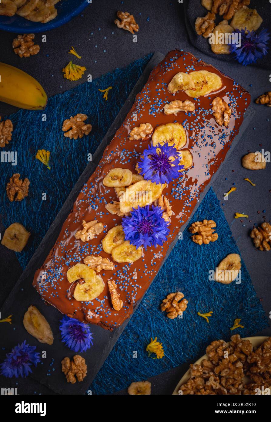 Pane di banana con cioccolato, patatine di banana e noci, decorato con fiori di mais, vegan, fotografia alimentare Foto Stock