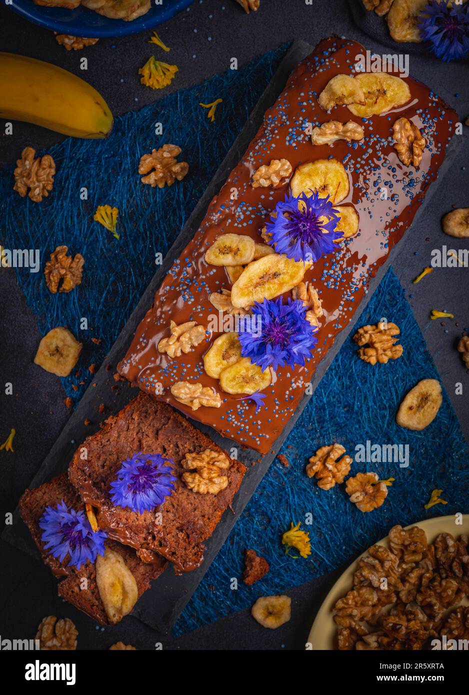 Pane di banana tagliato con cioccolato, patatine di banana e noci, decorato con fiori di mais, vegan, fotografia alimentare Foto Stock