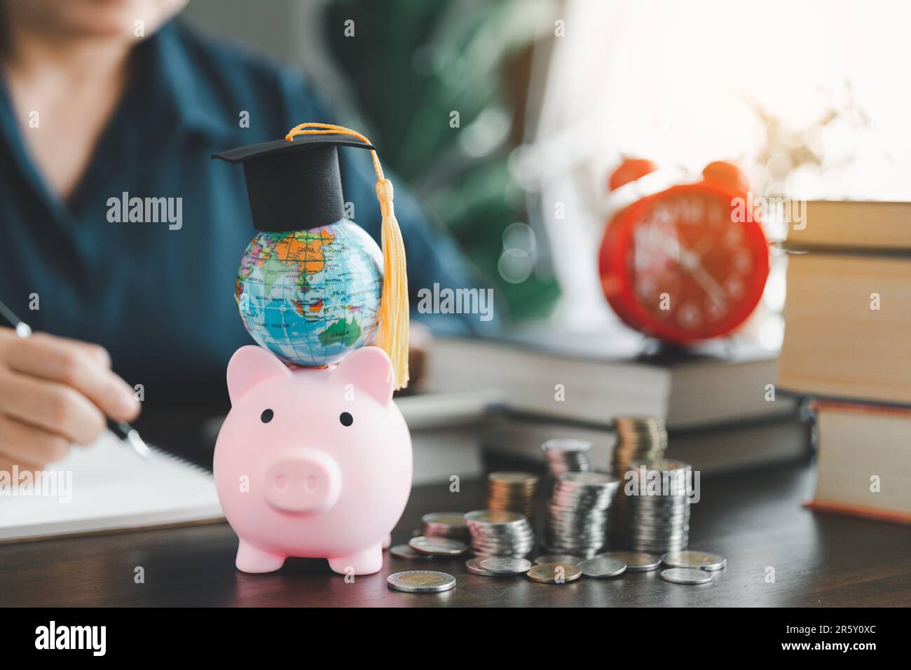 Tappo graduato con globo su banco rosa con pila di monete. Concetto di risparmio per borse di studio per studiare all'estero a livello universitario. Financi Foto Stock