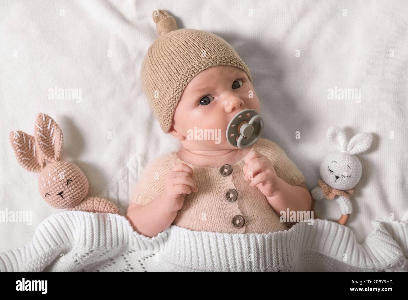 Bambino neonato carino con succhietto e giocattoli su plaid in maglia bianca, vista dall'alto Foto Stock