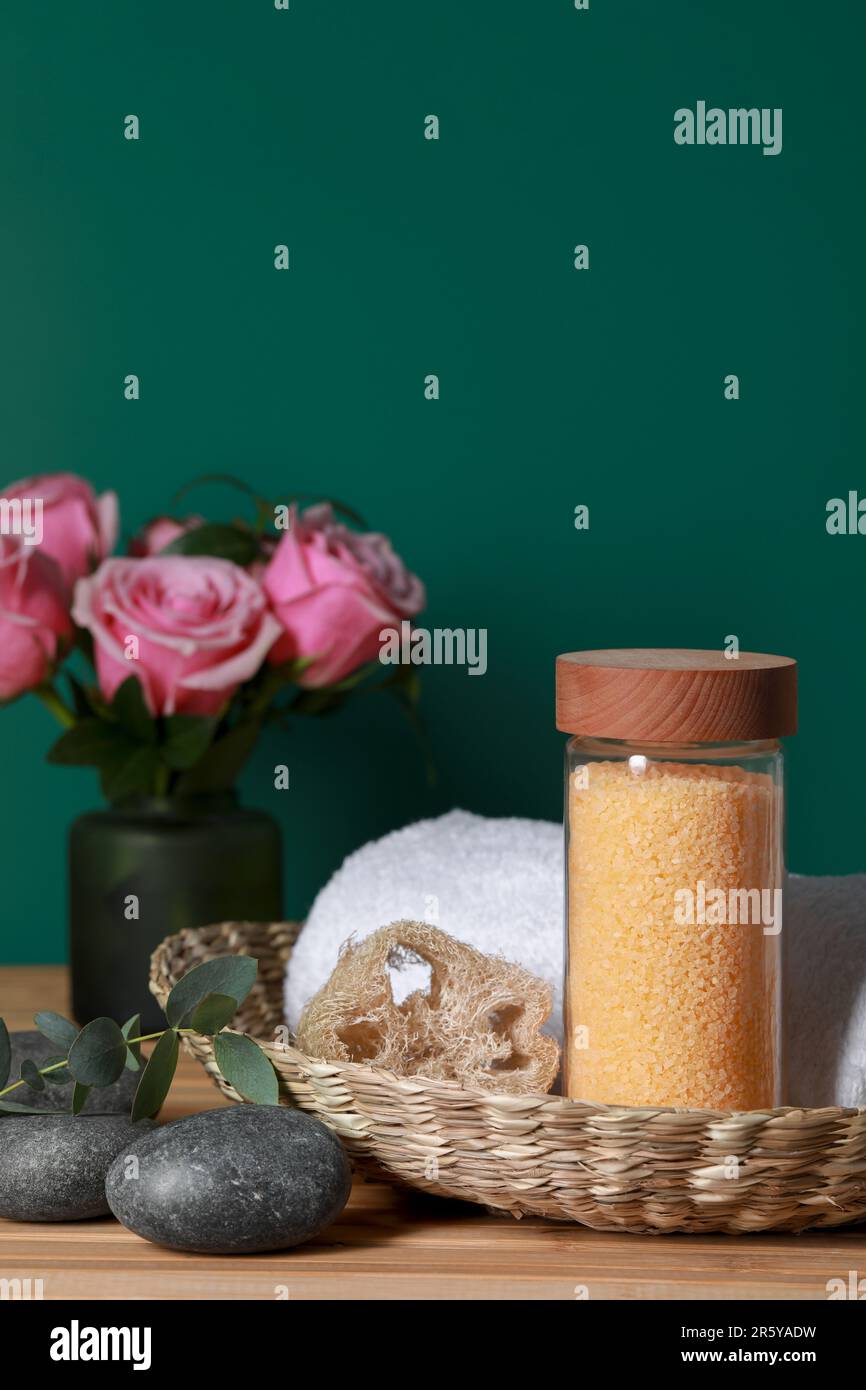 Bella composizione con sale marino, rose e diversi prodotti termali su tavolo di legno vicino parete verde, primo piano Foto Stock