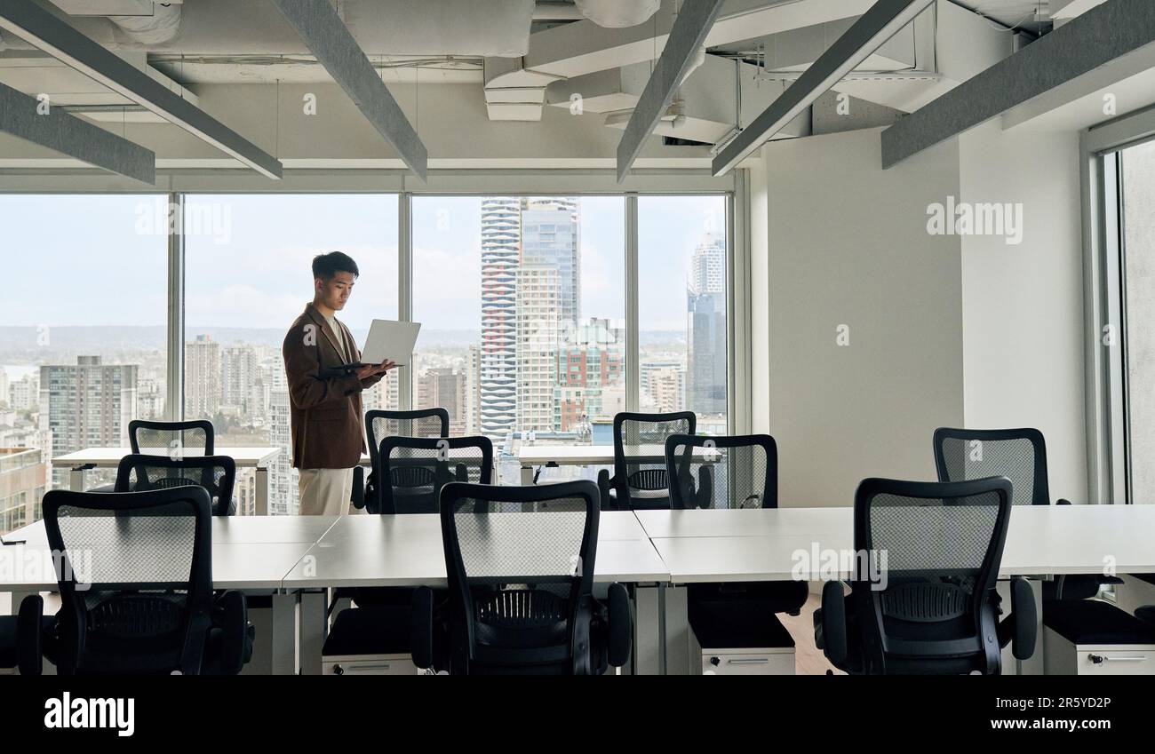 Giovane uomo d'affari asiatico serio che lavora su un notebook in ufficio. Foto Stock