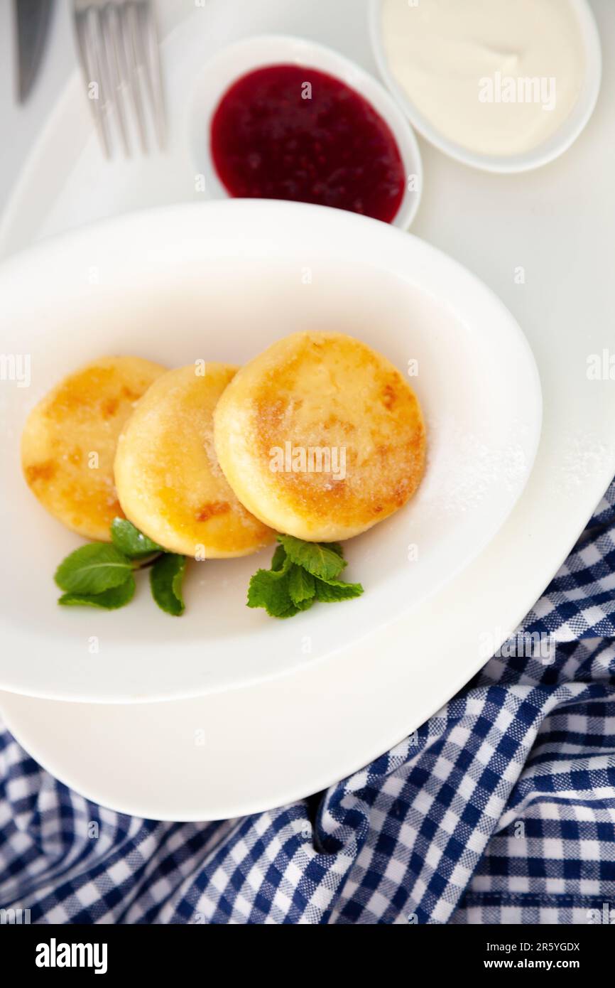 Frittelle di formaggio ricotta rotonda in un piatto bianco su sfondo blu. Cibo prima colazione. Cibo sano. Salsa di panna acida e menta. Primo piano vista dall'alto. Pasto dessert. Frittelle di ricotta al formaggio ricotta. Foto Stock