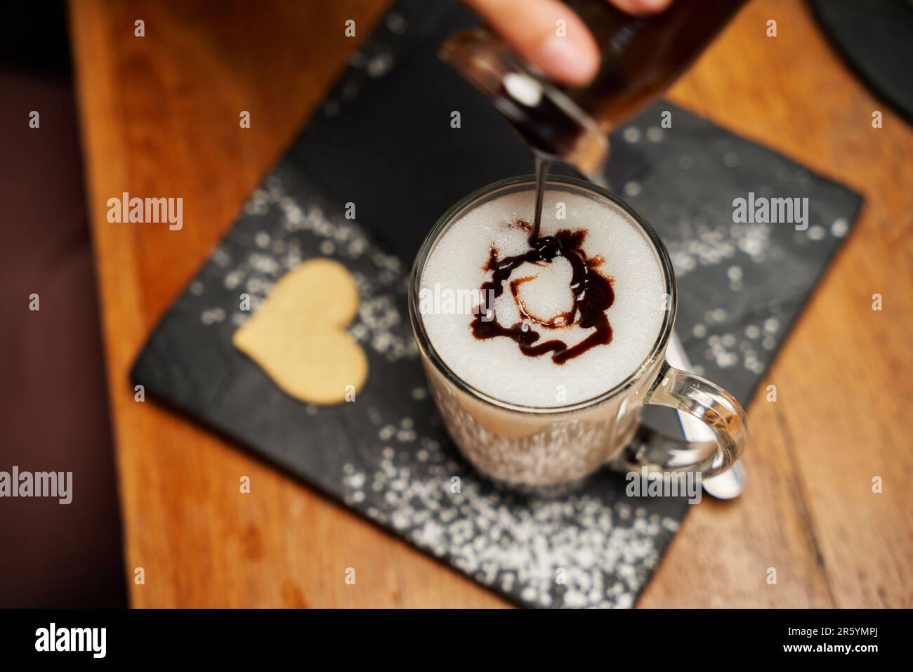 Primo piano di una giovane donna caucasica che versa sciroppo in una bevanda sul piatto a forma di cuore Foto Stock
