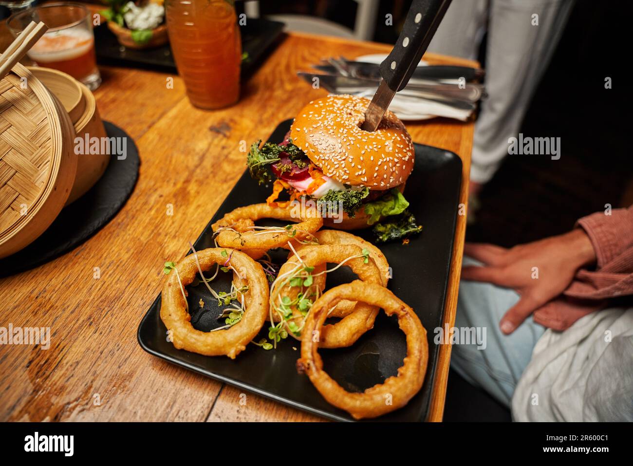 Primo piano di giovani amici multirazziali in abbigliamento informale che hanno hamburger al ristorante Foto Stock