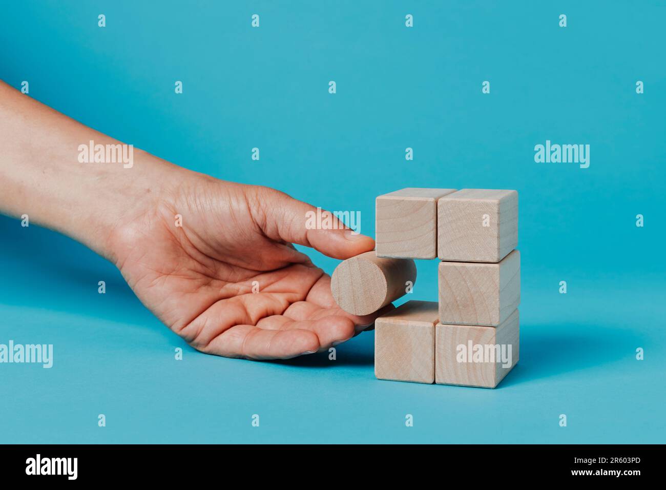 un uomo sta mettendo un blocco cilindrico in una pila di blocchi rettangolari, su uno sfondo blu Foto Stock