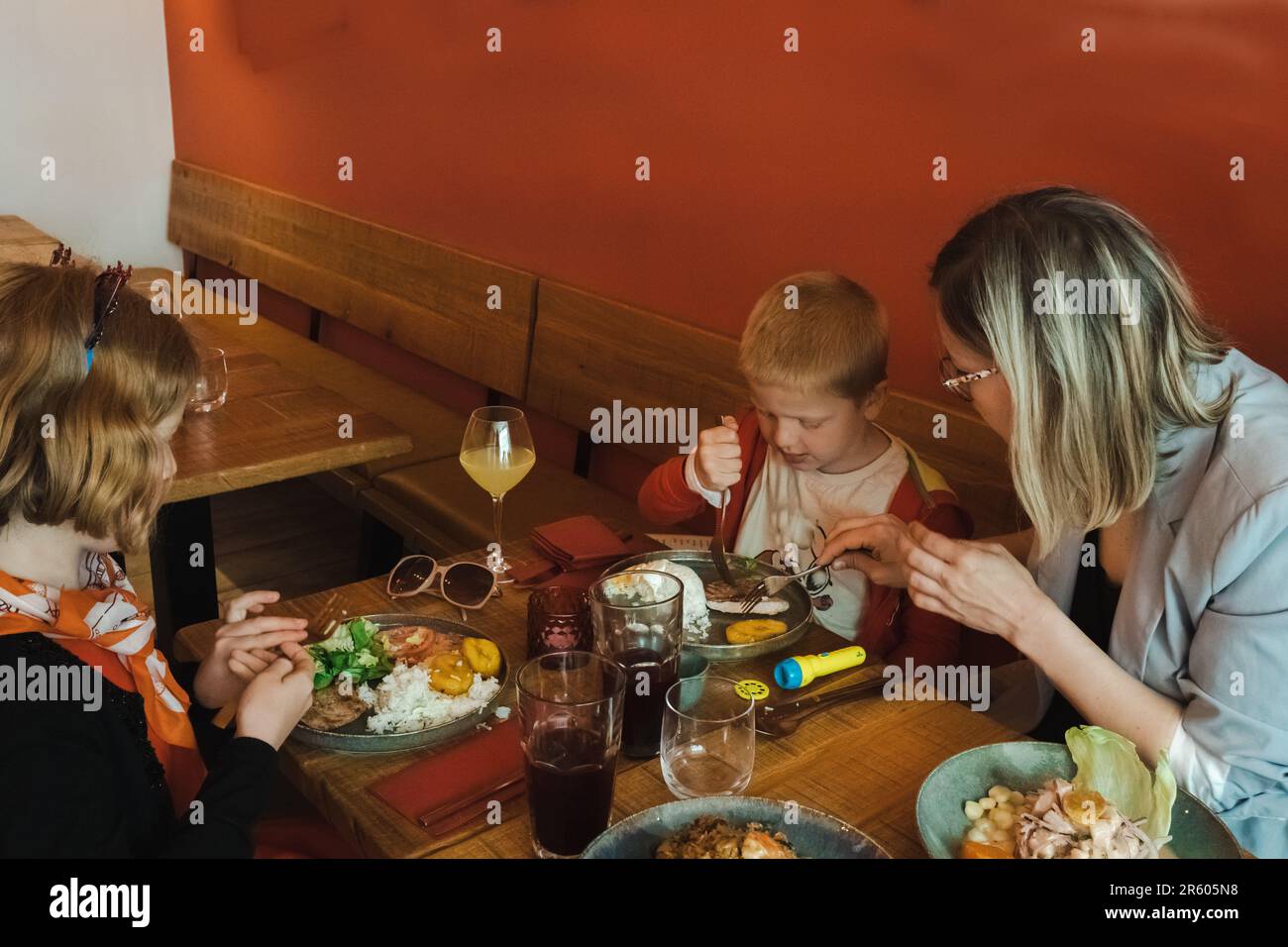 Pranzo di famiglia, madre con due bambini in un ristorante. Madre impegnata ad aiutare i bambini con il pasto. Foto Stock
