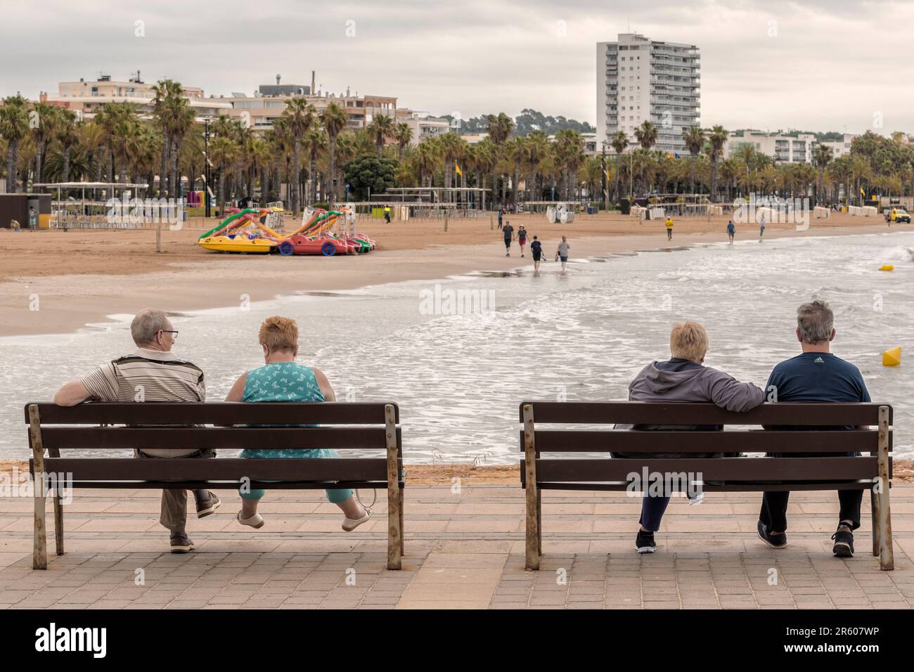 Due coppie seduti quattro su panchine sul lungomare della marina che si affaccia sulla spiaggia di Levante del Mar Mediterraneo a Salou, Tarragona, Spagna. Foto Stock