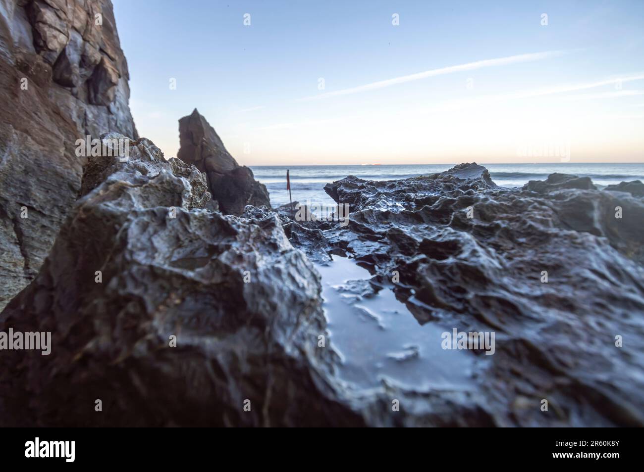 Pietre bagnate dalle onde del mare e bandiera rossa nell'oceano sullo sfondo, struttura con pietre e mare, concetto di onde del mare. Foto Stock