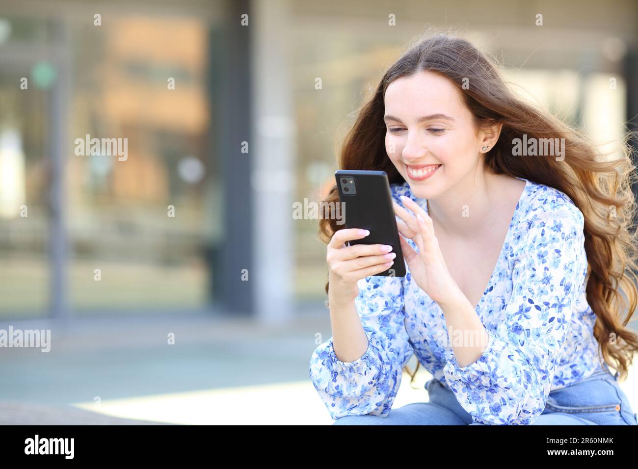 Donna felice seduta in strada utilizzando il telefono cellulare Foto Stock