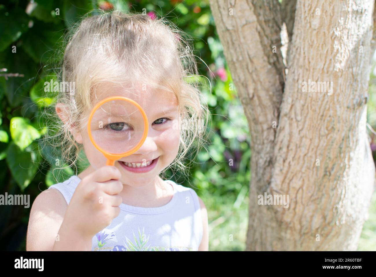 Carina ragazza caucasica sorridente con lente d'ingrandimento. Piccolo concetto di esploratore. Foto Stock