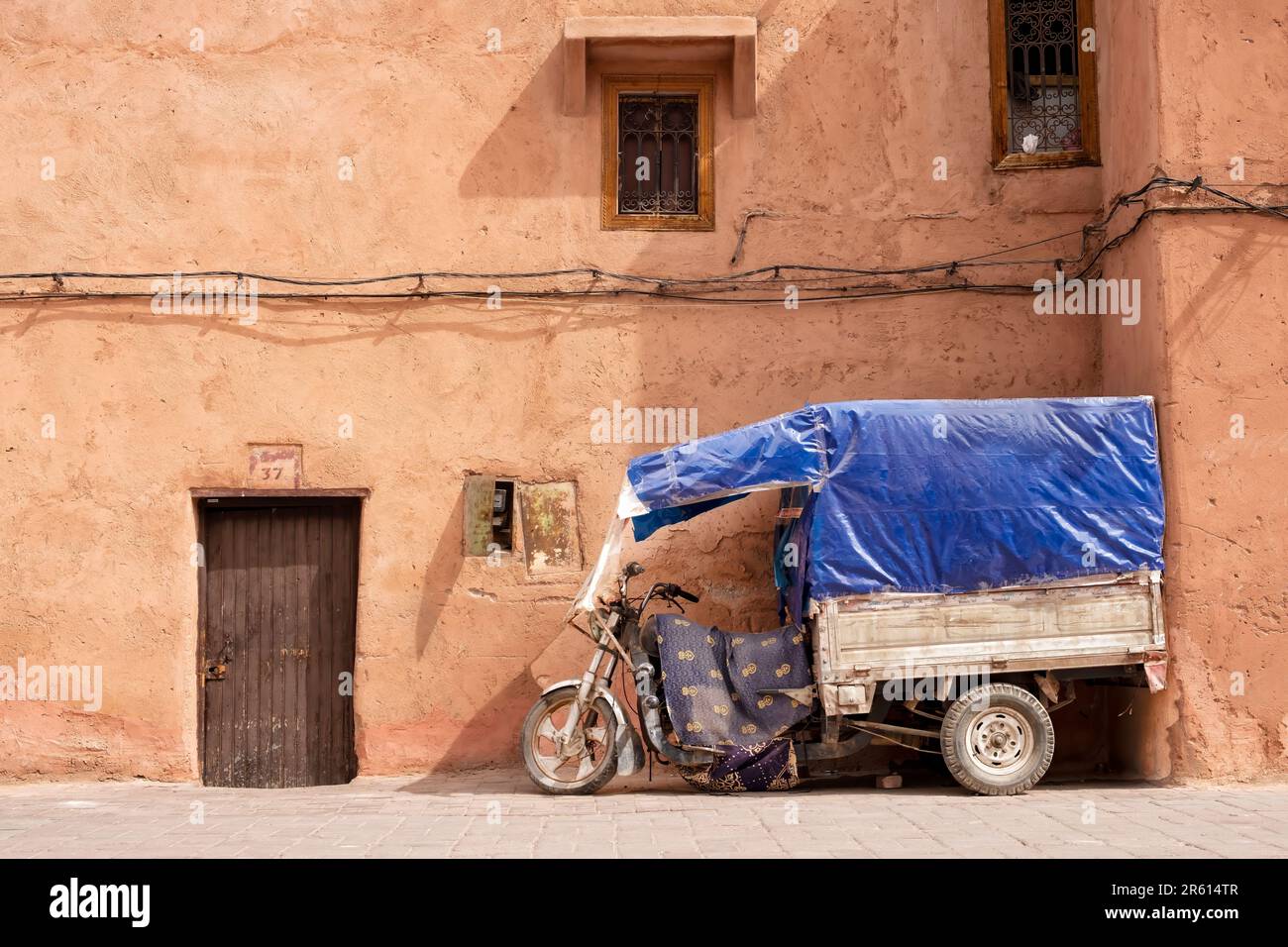 Un triciclo a motore ben usato con un rimorchio fisso e una tenda parcheggiata fuori da un vicolo nella Medina di Marrakech, Marocco. Foto Stock