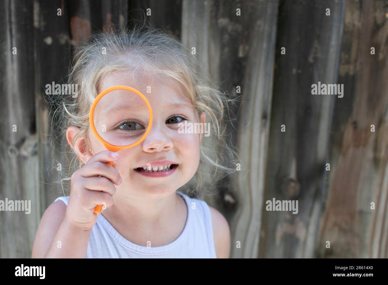 Carina ragazza caucasica sorridente con lente d'ingrandimento. Piccolo concetto di esploratore. Preschooler con lente d'ingrandimento Foto Stock