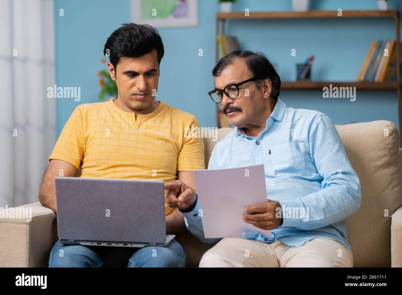 Padre anziano indiano con figlio adulto che disusa controllando alcuni documenti cartacei usando il laptop - concetto di informazione, paternità e. Foto Stock