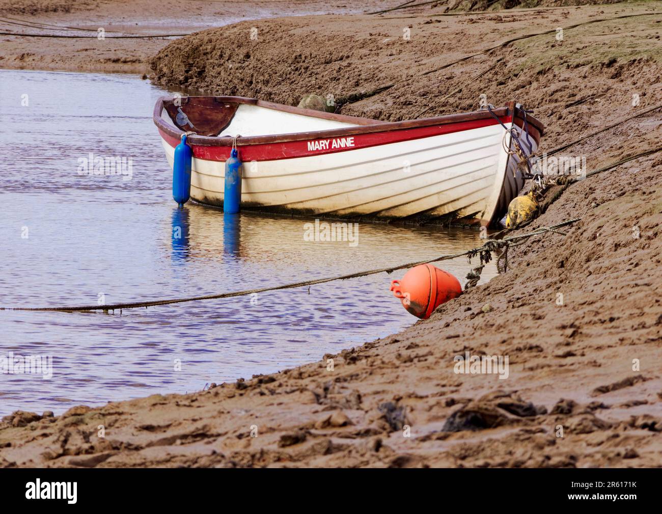 Bassa marea lungo New Cut a Blakeney, North Norfolk con una grande barca aperta lasciata in piedi sul fango in attesa della prossima marea di alluvione. Foto Stock